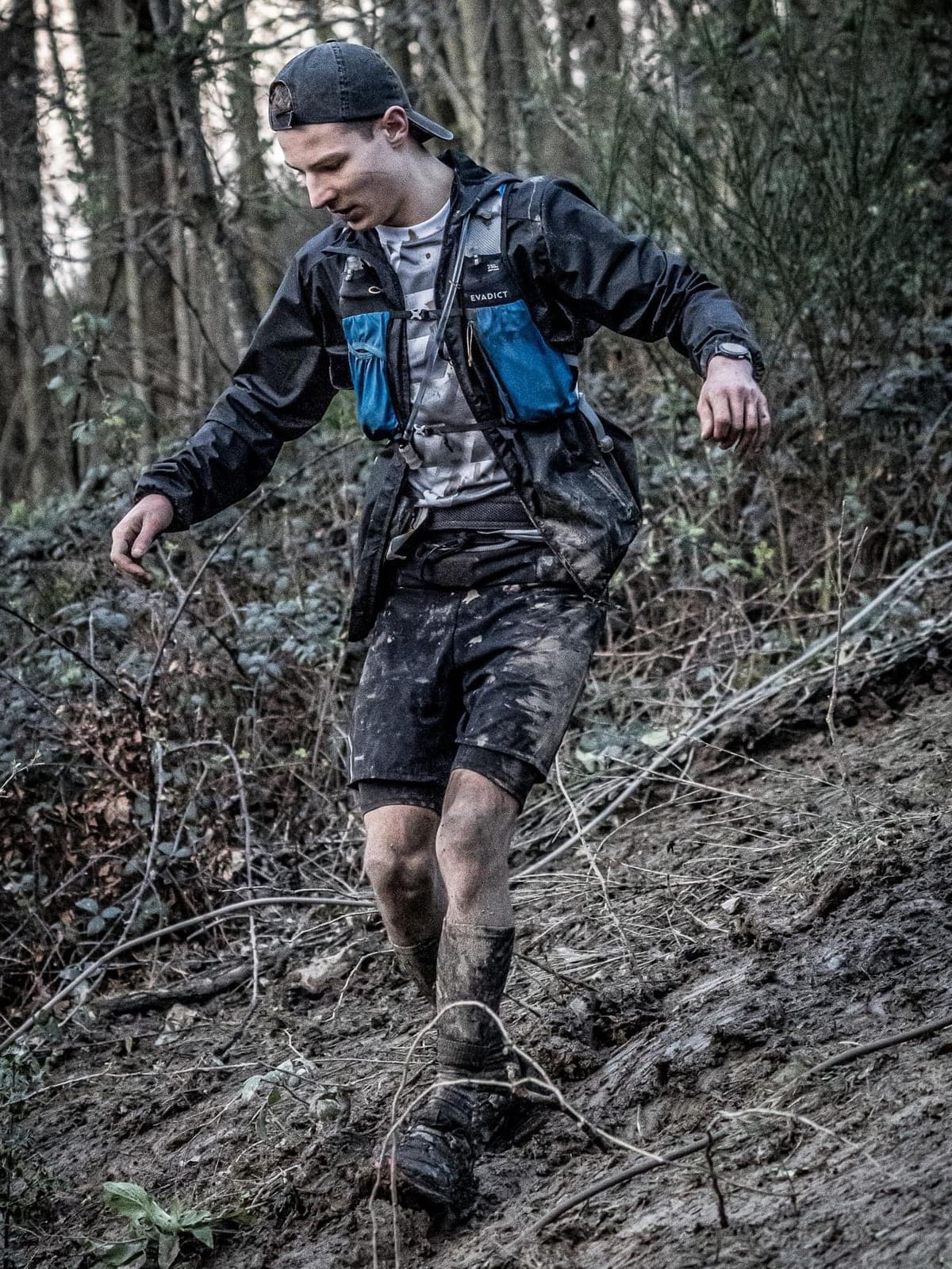 Un coureur du clan dévale une pente couverte de boue, en forêt